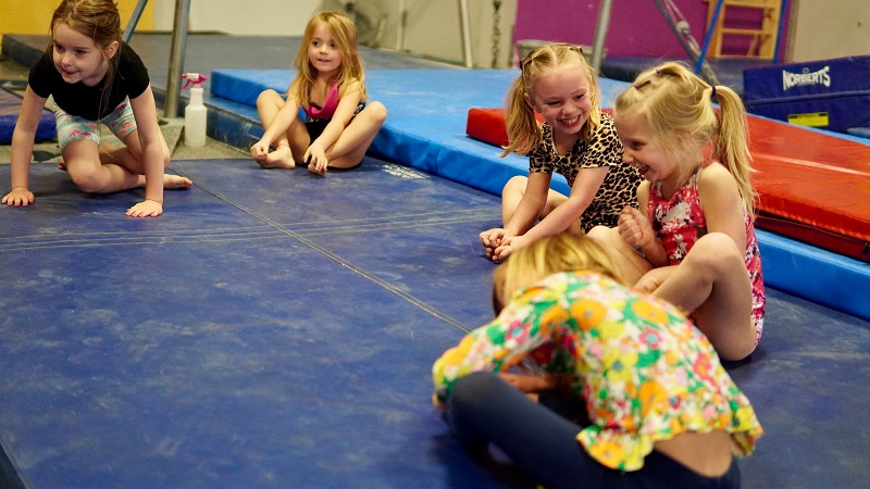 Young children in a gym sitting on a large mat